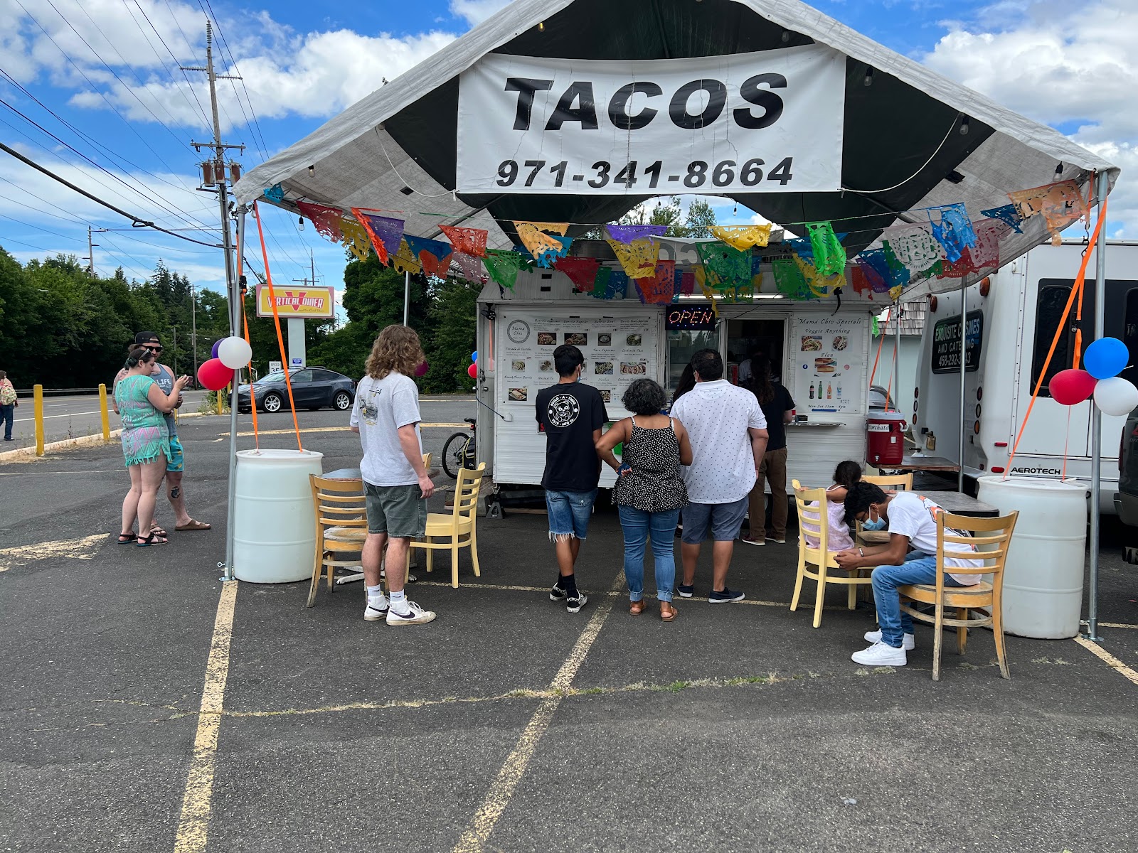 Customers gather outside the taco stand under a large canopy on a cloudy day.